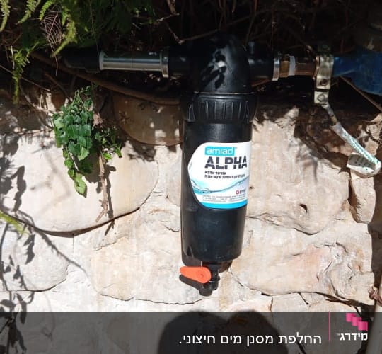 מסנן מים שחור עם ברז כתום על קיר אבן